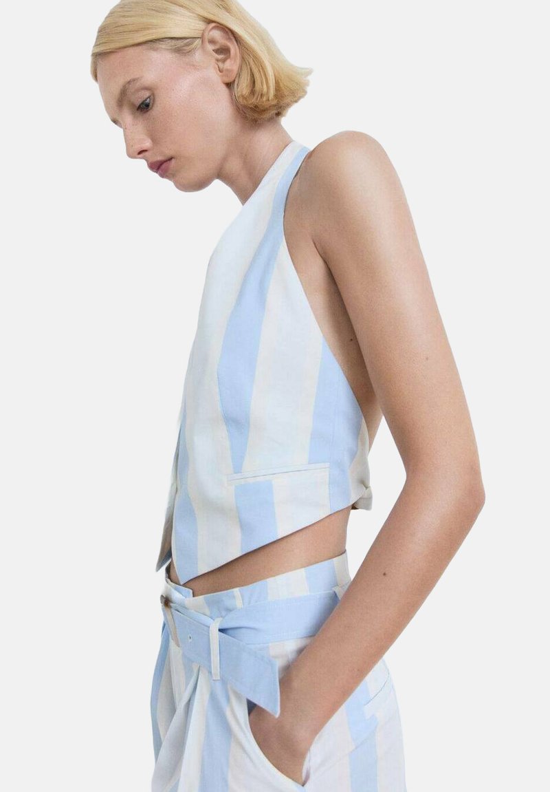 Prugasta brezrokavna majica v svetlo modri in beli barvi iz bombaža, z obrezanim krojem in stranskimi žepi, v kombinaciji z usklajenimi hlačami s pasom.