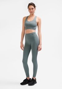 Set di reggiseno sportivo e leggings grigi con texture a coste, dettagli con logo e accenti turchesi, abbinato a scarpe da ginnastica nere.