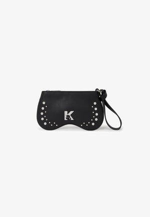 Bolso de mano de cuero negro con un diseño ondulado, adornado con tachuelas circulares blancas y un logo plateado centrado en la parte delantera. Incluye una correa para la muñeca.