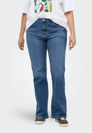 Blue denim flared jeans with a mid-rise waist, featuring five pockets and a button closure. Worn with a white graphic t-shirt and brown sneakers.