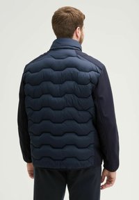 Doudoune marine avec un design matelassé hexagonal au dos, associée à des manches unies de couleur sombre. Elle dispose d'un col haut et d'une texture lisse.