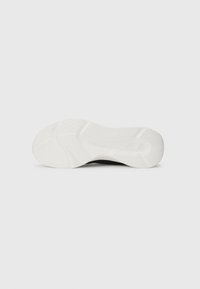 White sole of a sneaker shown from the bottom, featuring textured grip patterns and a subtle logo near the heel.