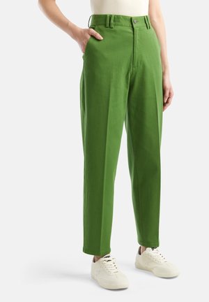 Osoba nosząca zielone, wysokie w talii, proste spodnie z kieszeniami, w połączeniu z białymi trampkami i białym, wsuniętym topem.