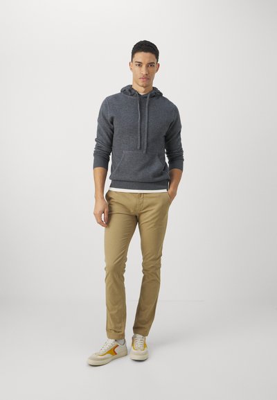 Hanorac gri cu glugă, dotat cu buzunar tip kangaroo, asortat cu pantaloni chinos slim-fit bej și adidași ușori cu accente galbene.
