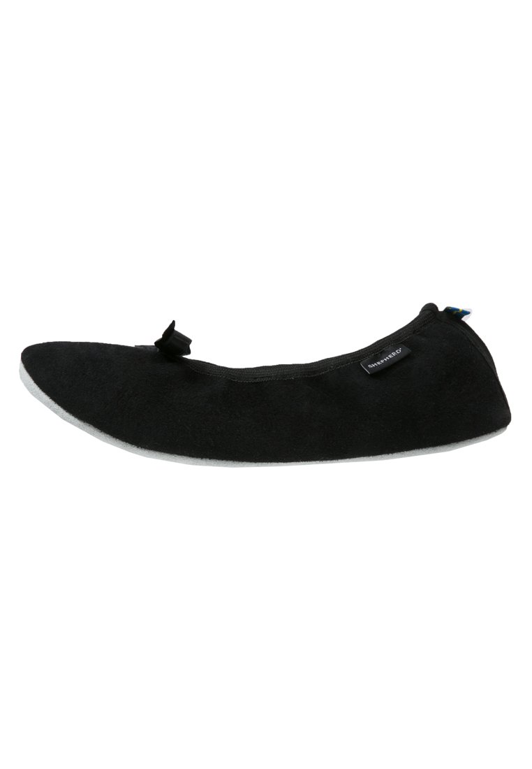 Black slipper with a soft suede upper, rounded toe, flat grey sole, and a decorative bow detail at the front; minimalistic design.
