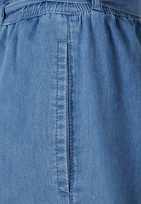 Gros plan sur un tissu en denim bleu avec une ceinture élastique et une poche latérale verticale avec des détails de couture.