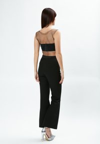 Zwarte high-waisted broek gecombineerd met een doorzichtige, mesh top met polkadots, aangevuld met zilveren hakken.