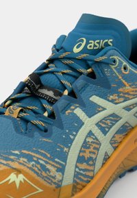 Blauwe en tealkleurige sportschoen met oranje accenten, gestructureerde bovenkant, prominent ASICS-logo en een patroonontwerp aan de zijkanten.