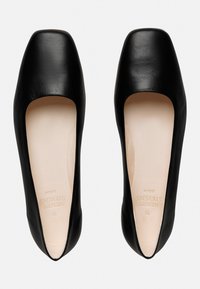 Schwarze Lederflats mit quadratischer Zehenform und offenen Seiten. Glatte Textur und minimalistisches Design. Das Innere verfügt über einen hellen Futter.