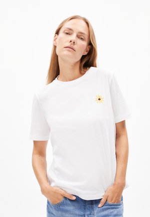 Weiße Baumwoll-T-Shirt mit kurzen Ärmeln, auf der linken Brust mit einer kleinen gelben Blumenstickerei verziert. Glatte Textur und klassischer Schnitt.