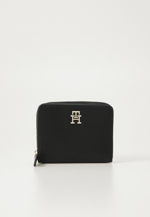 Svart zippered plånbok i slät läder. Har ett guldlogo-ackcent på framsidan. Kompakt rektangulär form, minimalisk design.
