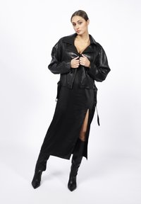Czarna skórzana krótka kurtka z wyciętym kołnierzem, zestawiona z długą czarną satynową sukienką z wysokim rozcięciem na udzie. Czarne kozaki do kolan z czubkiem.