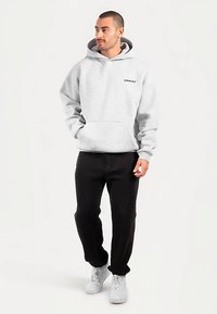 Grijze hoodie van een katoenmengsel, met een kangaroozak aan de voorkant en een capuchon met trekkoord. Gecombineerd met zwarte broek en witte sneakers.