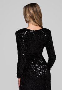 Robe noire à sequins avec manches longues, encolure ronde et silhouette ajustée. La texture est lisse avec des sequins réfléchissants sur toute la surface.