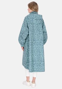 Palton lung, supradimensionat, de culoare teal, cu un model leopard în albastru deschis. Țesătura pare netedă, cu glugă și mâneci adunate.