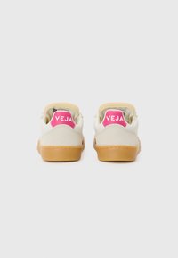 Lyse beige joggesko med semsket overflate, brune gummisåler og lys rosa "VEJA"-merking på hælen. Glatt tekstur med lavt design.