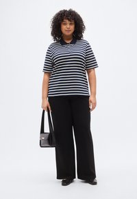 Ριγέ μπλε ναυτικό και λευκό πόλο πουκάμισο συνδυασμένο με μαύρο παντελόνι φαρδύ. Το μοντέλο κρατά μικρή μαύρη τσάντα χιαστί. Λείο ύφασμα και χαλαρή εφαρμογή.