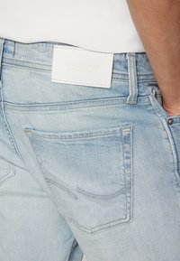 Ljusblå denimjeans med ett vitt lädermärke märkt "JACK & JONES." Har bakfickor och synliga sömnadsdetaljer.