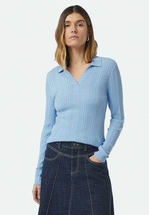 Light blue ribbed knit pullover with a V-neck and collar. Worn with a dark denim skirt featuring visible stitching and pockets.