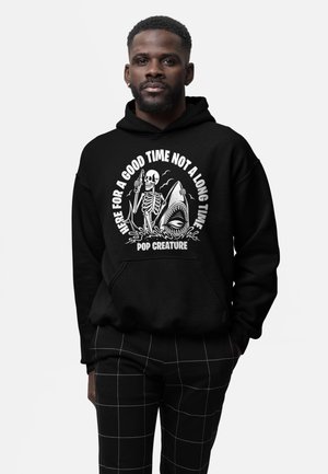 Homme portant un sweat à capuche noir avec un squelette tenant une bouteille à côté d'un requin et le texte « Ici pour passer un bon moment, pas pour longtemps » et « Pop Creature ».