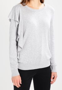 Hellgrauer Langarmpullover mit Rundhalsausschnitt, der Rüschendetails auf der linken Seite sowie gerippte Bündchen und Saum aufweist. Glatte Textur.