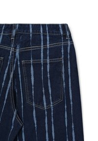 Jeans in denim blu scuro con strisce verticali di tie-dye blu chiaro, tasca posteriore visibile e cuciture a contrasto su uno sfondo bianco.