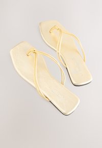 Goldene flache Sandalen mit quadratischer Zehenpartie und dünnen Riemen, mit strukturiertem Finish und minimalistischen Design. Die Sohle ist glatt und schwarz.