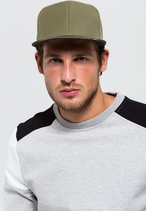 Olijfgroen pet met een vlakke rand, gemaakt van textuurstof, gecombineerd met een grijze sweatshirt met zwart-wit kleurblokken op de mouwen.