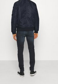 Marinblå bomberjacka i slät tyg, med ribbad nederkant och svarta applikationer, i kombination med mörka jeans och svarta sneakers med vita sulor.