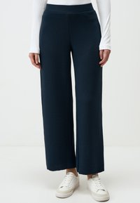 Navy brede broek gemaakt van ribbelstof, met een hoge tailleband en een losse pasvorm, gecombineerd met witte sneakers.