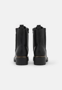 Botas de tobillo negras con un acabado de cuero suave, cremalleras laterales y una banda de acento dorada en el tacón. Suelas sturdas con relieve para mayor tracción.