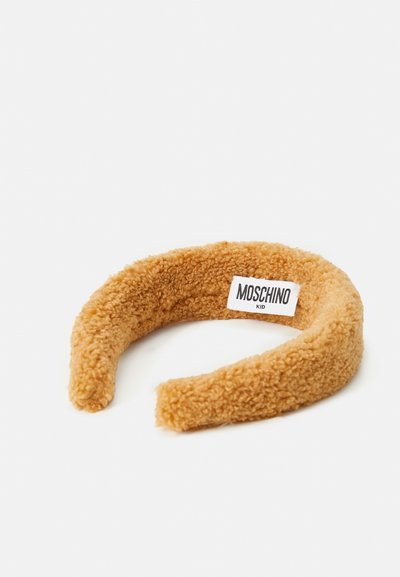Rudas pūkuotas galvos apdangalas, pagamintas iš tekstūruotos medžiagos, su švelniu, pūkuotu paviršiumi ir balta etikete, kurioje užrašyta "Moschino Kid", esančia vidinėje pusėje.
