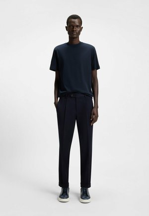 Navy crew-neck t-shirt with short sleeves paired with tailored navy trousers. Model wears dark sneakers with white soles.