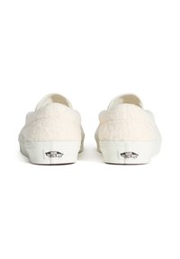 Krémové slip-on tenisky s texturovaným, měkkým svrškem, bílými gumovými podrážkami a malým černým logem na patě.