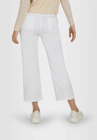 White wide-leg jeans with a high waist, featuring back pockets and a clean finish. Paired with light-colored sneakers.
