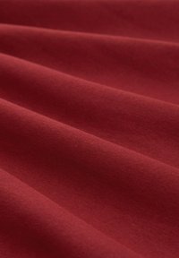 Tessuto rosso che presenta una superficie liscia con pieghe visibili. Il materiale sembra morbido, con una finitura opaca e una colorazione uniforme.