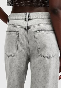 Jeans de mezclilla gris con una textura desgastada, cintura alta, dos bolsillos traseros y costuras en contraste a lo largo de las costuras.