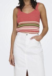 Dziergany top na ramiączkach w koralowym kolorze z poziomymi paskami w kolorze kremowym, zielonym i różowym; zestawiony z białą spódnicą jeansową z przednim rozcięciem.