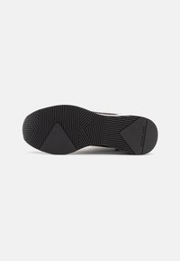 Semelle de chaussure en caoutchouc noir avec des motifs texturés, comportant des rainures horizontales et verticales pour l'adhérence et la stabilité. Nom de la marque visible sur le côté.
