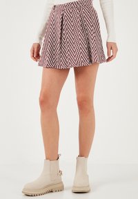 Gonna corta e plissettata in un motivo a spina di pesce bordeaux e bianco, abbinata a stivaletti beige con suola robusta.