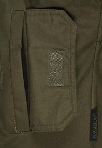 Close-up of olive green fabric pocket with Velcro flap and black rectangular Navajo brand tag on the side.