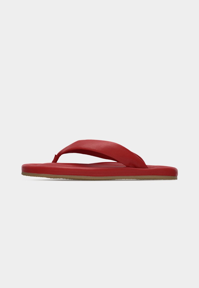 Czerwona klapka typu japonki z wyściełanym paskiem między palcami i płaską podeszwą na jasnoszarym tle.