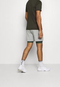Conjunto masculino que incluye una camisa de manga corta verde oscura y pantalones cortos gris claro. Zapatillas deportivas blancas con acentos negros y calcetas a rayas.