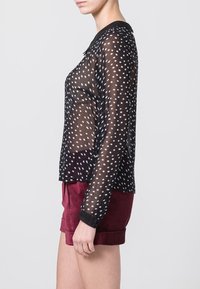 Blusa negra transparente con lunares blancos, de mangas largas y con cuello. Combinada con pantalones cortos burdeos. Tejido suave y ligero.