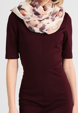 Vrouw draagt een donkerpaars nauwsluitende jurk met mouwen tot aan de elleboog en een lichte sjaal met een bloemenpatroon om haar nek gewikkeld.