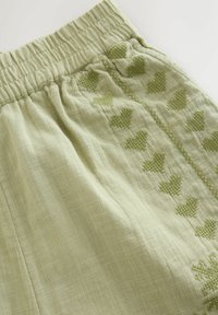 Helle grüne Leinen-Shorts mit elastischem Bund und aufgestickten Herzmustern in einem dunkleren Grün entlang der Seitennähte.