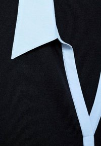 Light blue pointed collar over black textured fabric, close-up view of shirt neckline and collar details.