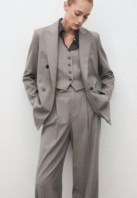 Traje gris a medida hecho de una tela de textura fina, que presenta un blazer de doble botonadura, un chaleco con botones y pantalones anchos.