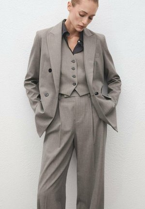 Costume gris taillé en tissu à texture fine, comprenant un blazer croisé, un gilet avec des boutons et un pantalon large.