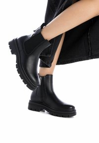 Botas de cuero negro hasta el tobillo con paneles elásticos en los laterales, suela de goma texturizada y un detalle de cremallera. Acabado suave con una puntera redondeada.
